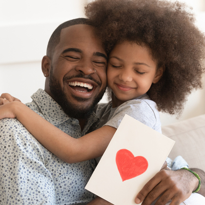 Happy Black girl with afro hugging smiling Black man, with man holding card with heart on it