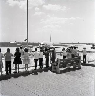 Photo of children watching a plane take off at the airport, circa 1960's. 