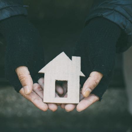 A person wearing black fingerless gloves holds a cardboard cutout in the shape of a house