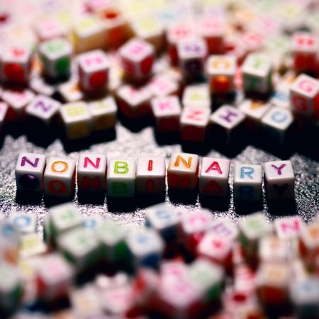 multicolored beaded letters on a surface, the center of the photo has the word nonbinary spelled with different colors.